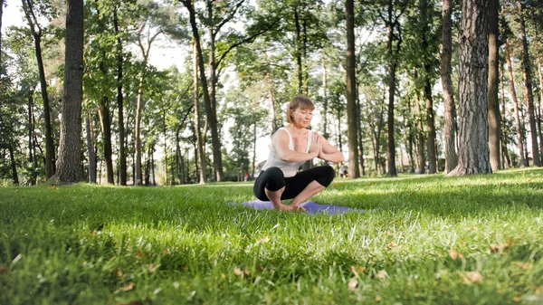 Zdjęcie uśmiechniętej kobiety robi jogi i ćwiczeń fitness. Ludzie w średnim wieku dbają o swoje zdrowie. Harmonia ciała i umysłu w przyrodzie — Zdjęcie stockowe