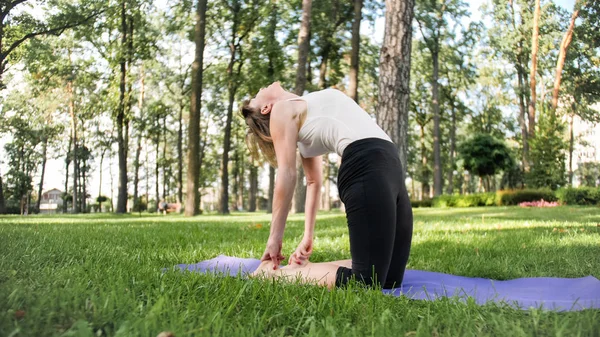 Obraz połowie wieku uśmiechnięty szczęśliwy kobieta medytuje i robi ćwiczenia jogi na trawie w lesie. Kobieta dbająca o jej zdrowie fizyczne i psychiczne podczas pracitising fitness i rozciągania w parku — Zdjęcie stockowe