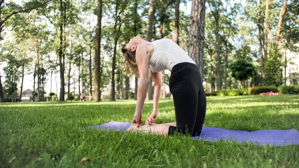 Photo of smiling happy woman 40 years old doing yoga exercises on fitness mat at forest. Harmony of human in nature. Middle aged people taking car of mental and physical health