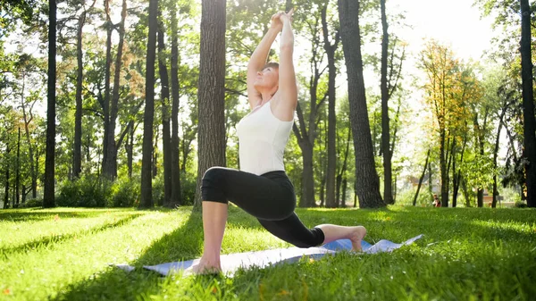 Afbeelding van mid Aged glimlachende gelukkige vrouw mediteren en doen van yoga oefeningen op gras in het bos. Vrouw het verzorgen van haar lichamelijke en geestelijke gezondheid terwijl pracitizing fitness en stretching in Park Rechtenvrije Stockafbeeldingen