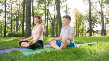 Parkta çim yoga asana pratik onu genç erkek oğlu ile anne fotoğrafı. Aile ormanda fitness ve spor outtodr yapıyor
