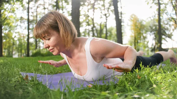 Foto de una mujer de mediana edad practicando yoga o fitness sobre hierba verde fresca en el parque. Salud física y mental femenina. Persona en meditación y armonía pf cuerpo y alma — Foto de Stock