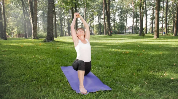Photo of middle aged smiling woman practising yoga asana. Persong meditating in nature. Balance and harmony of body and mind