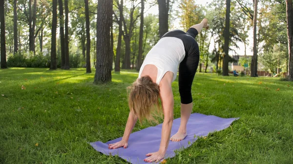 Zdjęcie uśmiechniętej szczęśliwej kobiety 40 lat robi ćwiczenia jogi na mat fitness w lesie. Harmonia ludzkiej natury. Ludzie w średnim wieku, biorąc samochód zdrowia psychicznego i fizycznego — Zdjęcie stockowe