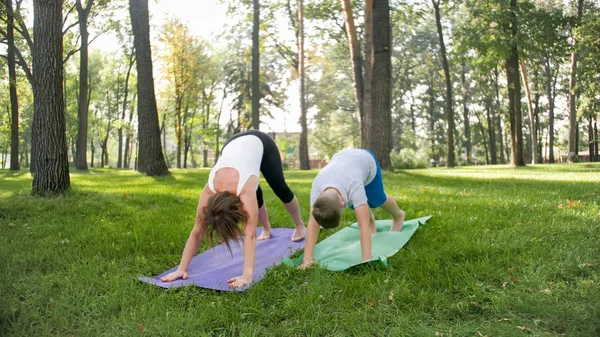 Zdjęcie w średnim wieku kobieta z 12 lat nastoletniego chłopca praktykujących jogi i medytacji w parku. rodzinne relaks i fitness na łonie natury — Zdjęcie stockowe