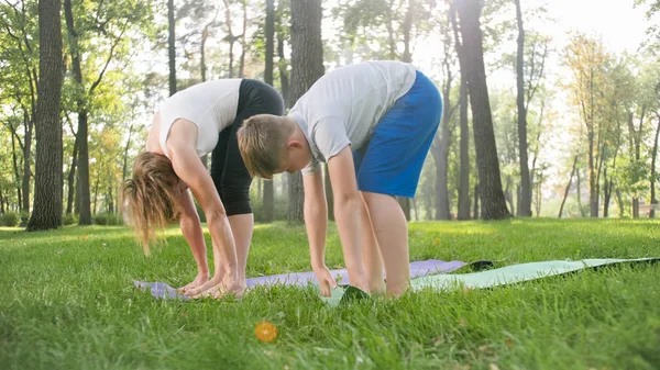 Zdjęcie w średnim wieku kobieta nauczania jej studenta w klasie jogi w parku. Woamn z nastoletnim chłopcem praktykujący fitness, medytacja i Joga na trawie w lesie — Zdjęcie stockowe