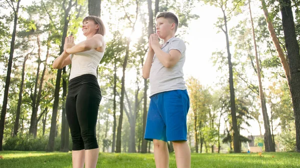Foto van tiener jongen doet yoga met zijn moeder op grass Park. Familie doet fitness en Stretching oefeningen samen bij forest — Stockfoto