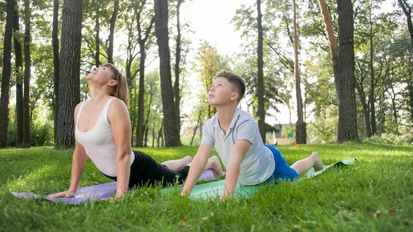 Zdjęcie w średnim wieku matki z jej nastoletniego chłopca dziecko robi joga i ćwiczenia oddechowe w parku. Rodzina dbając o THIR zdrowia psychicznego i fizycznego podczas uprawiania sportu — Zdjęcie stockowe