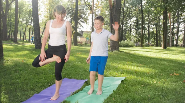 Zdjęcie matki z jej nastoletniego chłopca syna praktykujący jogę Asana na trawie w parku. Rodzina robi fitness i sportu outtodr w lesie — Zdjęcie stockowe