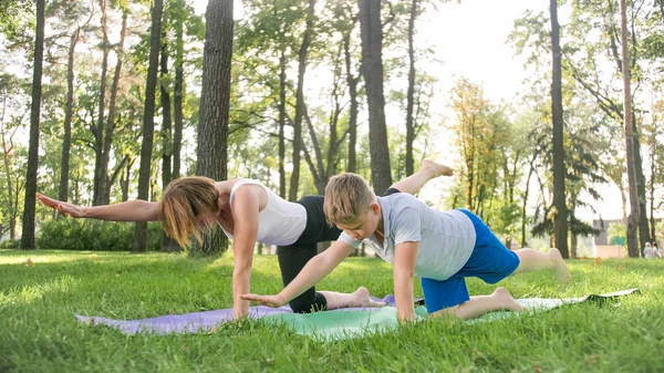 Wizerunek kobiety w średnim wieku nauczania nastoletniego chłopca robi jogę i fitness na trawie w parku. Rodzina dbając o ich zdrowie — Zdjęcie stockowe