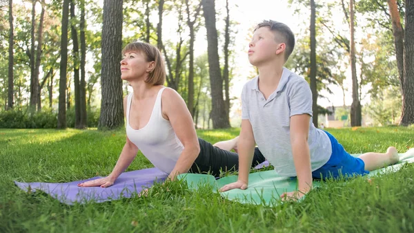 Zdjęcie w średnim wieku kobieta nauczyciel jogi lub guru nauczania nastoletniego chłopca robi jogi. Kobieta z chłopcem medytacji i rozciągania na trawie w parku — Zdjęcie stockowe
