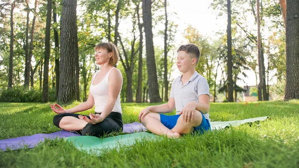 Wizerunek kobiety w średnim wieku nauczania nastoletniego chłopca robi jogę i fitness na trawie w parku. Rodzina dbając o ich zdrowie — Zdjęcie stockowe