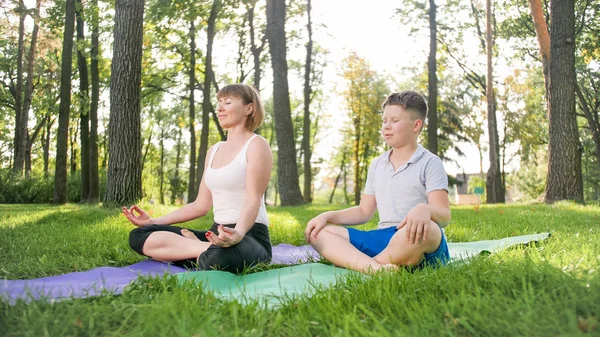 Zdjęcie w średnim wieku kobieta nauczania jej studenta w klasie jogi w parku. Woamn z nastoletnim chłopcem praktykujący fitness, medytacja i Joga na trawie w lesie — Zdjęcie stockowe