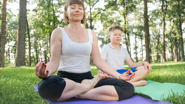 Zdjęcie w średnim wieku kobieta z 12 lat nastoletniego chłopca praktykujących jogi i medytacji w parku. rodzinne relaks i fitness na łonie natury — Zdjęcie stockowe