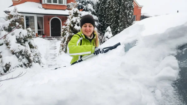 Closeup lövés boldog nő a kabátot tisztítás hóval borított autót használ havat kefe télen — Stock Fotó