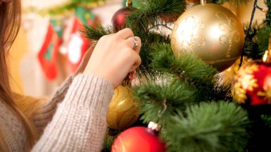Yün kazak süsleyen noel ağacını süsleyen genç kadının süs eşyası ve çelenklerle yakın çekim görüntüsü
