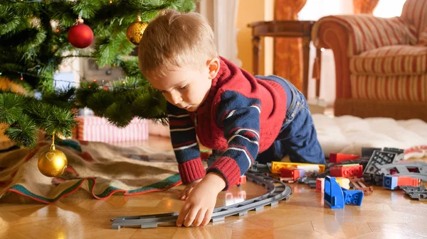 Küçük yürümeye başlayan çocuk bina demiryolu portresi ve Noel ağacı altında oyuncak tren ile oynarken — Stok fotoğraf