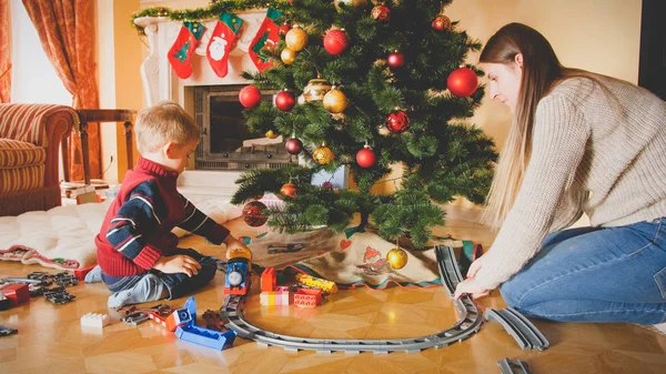 Foto tonificada de la familia jugando con el ferrocarril de juguete en el suelo en la sala de estar en la mañana de Navidad — Foto de Stock