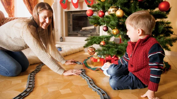 Família feliz brincando com o brinquedo ferroviário na manhã de Natal. Criança recebendo presentes e brinquedos no Ano Novo ou Natal — Fotografia de Stock