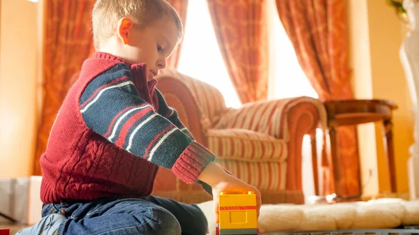 Porträtt av liten pojke leker med leksaker på trägolv i vardagsrummet mot stora fönster — Stockfoto