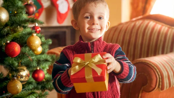 カメラにクリスマスプレゼントと箱を与える小さな笑顔の少年の肖像画。冬の休日やお祝いのための完璧な画像 — ストック写真