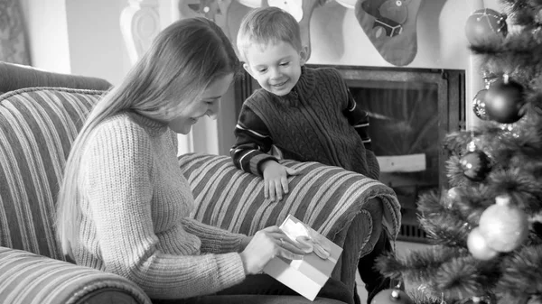 Svart och vitt porträtt av ung mor med sin lille son öppnings box med julklappar och presenter — Stockfoto