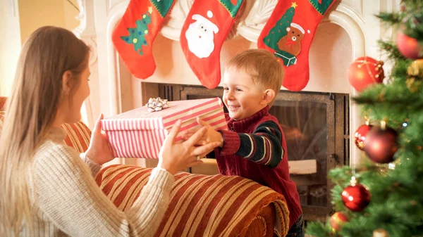 Портрет счастливого улыбающегося мальчика, дарящего большой ящик с рождественским подарком своей молодой матери — стоковое фото
