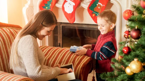 Portréja boldog mosolygó nő az ő kis fia nyitja díszdobozban karácsony reggel a nappaliban — Stock Fotó