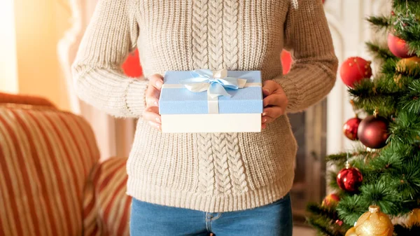 Close-up afbeelding van jonge vrouw met blauwe doos met lint boog tegen kerstboom in woonkamer — Stockfoto