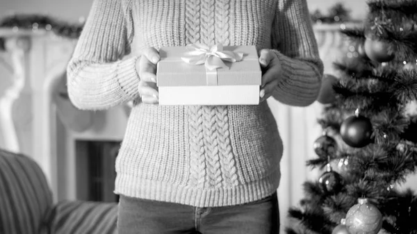 Immagine in bianco e nero di una giovane donna che tiene in mano la scatola regalo di Natale e la mostra in macchina fotografica — Foto Stock