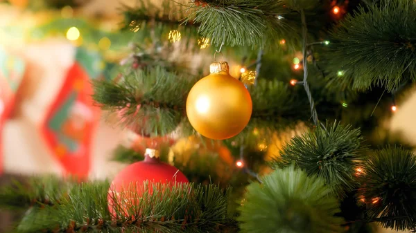 Closeup image of golden Christmas bauble hanging on fir tree at house living room against fireplace Stock Picture