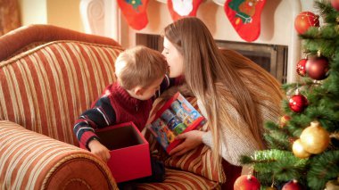 Genç annenin küçük oğlunu öpüp ona Noel hediyesi verdiği portresi. Kış tatilleri ve kutlamalar için mükemmel görüntü