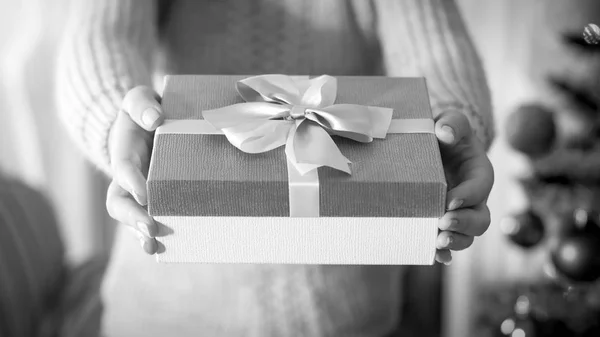 Imagen en blanco y negro de la mano femenina sosteniendo hermosa caja con regalo atado con cinta de lazo de seda —  Fotos de Stock