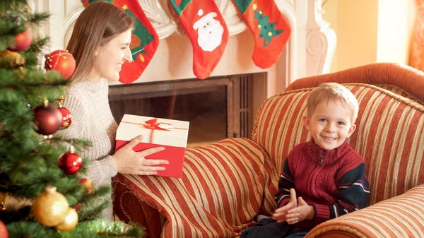 Retrato de menino sorridente feliz sentado em poltrona e esperando por sua mãe dando-lhe presente de Natal. Imagem perfeita para férias de inverno e celebrações — Fotografia de Stock