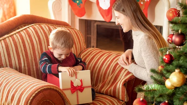 Foto do menino sorridente feliz abre caixa com presente de Natal e olhando para dentro. Mãe dando presente para seu filho no Ano Novo — Fotografia de Stock