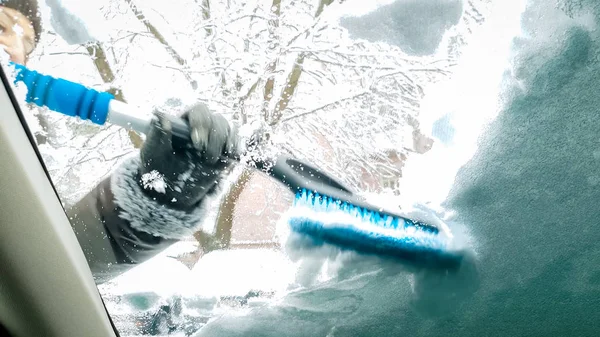 Fermer l'image à l'intérieur de la voiture couverte de neige. Dame souriante nettoyer le pare-brise et les essuie-glaces de son auto après tempête de neige avec brosse — Photo