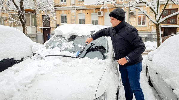 在霜冻的早晨，男人试图用刷子从雪中清理白色汽车的照片 — 图库照片