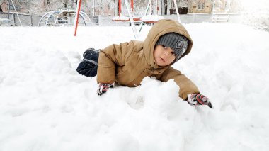Bej ceket büyüleyici çocuk Shot , kar fırtınası sonra karda oynamak için eğlenin. Parkta oyun alanında kar topları oynayın. Karda uzanmak gibi.