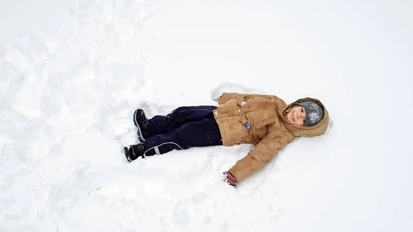 Imagen de niño lindo sonriente en abrigo, diviértete jugando en la nieve en el invierno después de la nevada. Juega en bolas de nieve en el parque infantil en el parque. Como tumbarse en la nieve — Foto de Stock