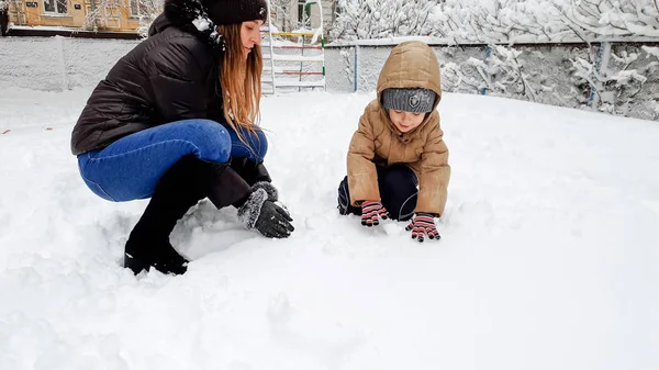 美丽的母亲与她可爱的儿子的照片有乐趣玩雪球在公园的游乐场 — 图库照片