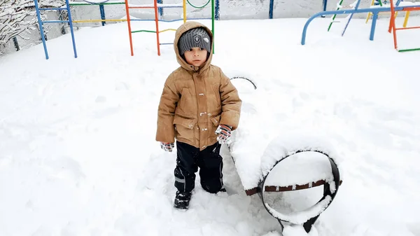 Närbild bild av leende lycklig söt pojke i beige päls och grå hatt, ha kul att spela i snön på vintern efter snöfall. — Stockfoto