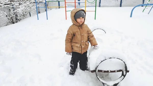 Tiro de menino divirta-se para jogar na neve após a nevasca. Jogar em bolas de neve no playground no parque . — Fotografia de Stock