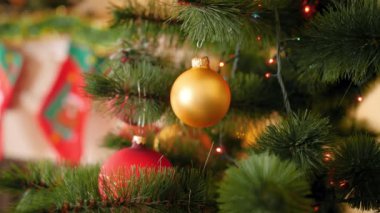 Dal üzerinde yanıp sönen ve parlayan Noel ışıkları çelenk karşı Noel ağacı dalı asılı altın bauble Closeup 4k video