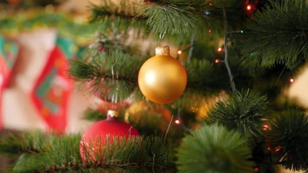 Closeup 4k video of golden bauble hanging on Christmas tree branch against blinking and glowing Christmas lights garland on branch — Stock Video