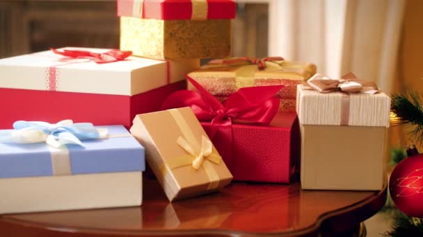 4K πλάνα από πολλά χριστουγεννιάτικα δώρα και δώρα από τον Άγιο Βασίλη σε ξύλινο τραπέζι και πολύχρωμο διακοσμημένο χριστουγεννιάτικο δέντρο στο σαλόνι — Αρχείο Βίντεο