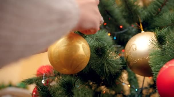 4k video de mujer joven en jersey decorando árbol de Navidad con bolas y bolas. Tiro perfecto para sus vacaciones de invierno y celebraciones — Vídeos de Stock