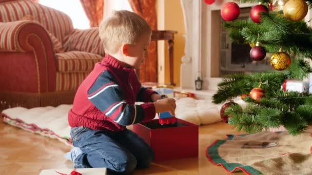 4k video de niño pequeño embalaje de juguetes en hermosa caja de regalo bajo el árbol de Navidad. Regalos y regalos para niños en las fiestas y celebraciones de invierno — Vídeos de Stock