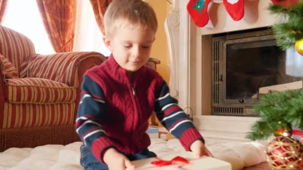 4k video de niño sonriente feliz sosteniendo y sacudiendo la caja de regalos con regalo de Navidad o regalo de Santa Claus. Niño recibiendo regalos y regalos en las vacaciones de invierno y celebraciones — Vídeo de stock