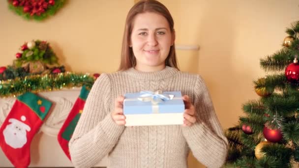 4k video van gelukkig glimlachende jonge vrouw toont doos met kerstcadeau in camera — Stockvideo