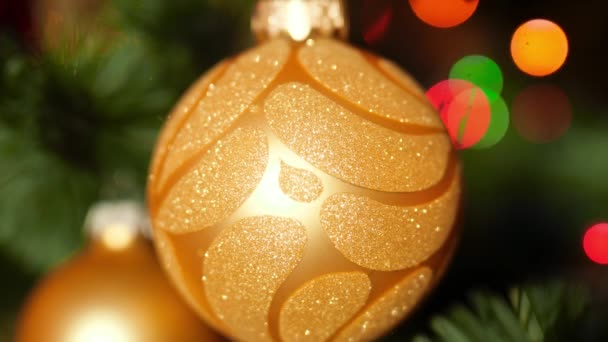 Närbild 4K bilder av gyllene utsmyckade småsak på julgran mot glödande färgglada ljus och girlander. Perfekt skott för din vintersemester och fester — Stockvideo